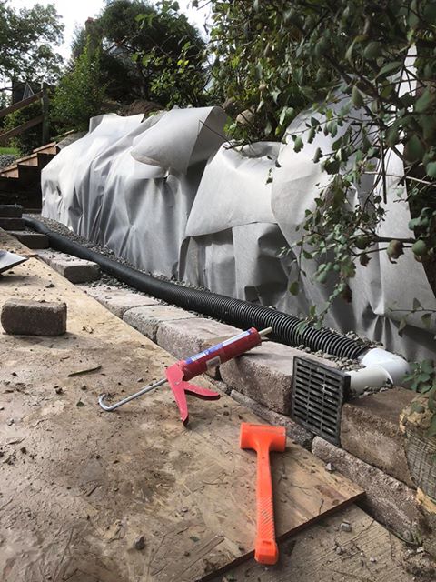 Perforated drain tile and filter fabric set behind a wall