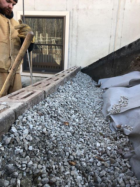 Clean stone backfill being shovelled against a foundation over filter fabric